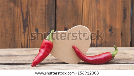 red chilly peppers with cardboard heart on wood background