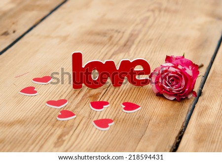 red-white rose and scattered flower petals and the word love on a rustic background