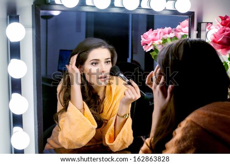 Woman in orange robe doing her makeup and watching in mirror