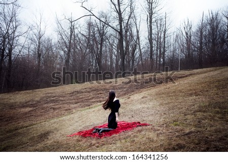 Woman in black dress and long hair sitting on red carpet in cold forest