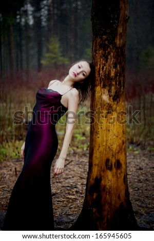 Pale woman in purple dress lying upon a tree