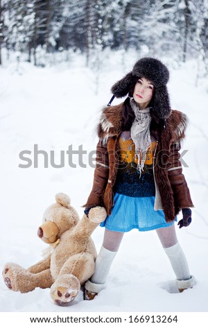 Woman in fur coat and ushanka with bear on white snow winter background