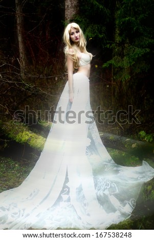 Blonde bride angel in long white skirt standing in dark forest