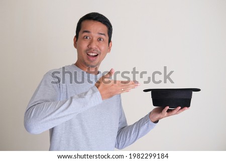 Adult Asian man laughing while holding a magician hat