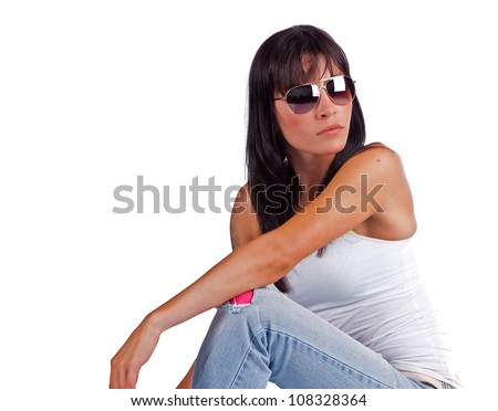 A beautiful young woman rests her arm on her knee while sitting down and chilling out with her sunglasses on.