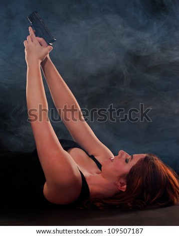 Laying on the ground under cover of the fog, a red headed woman lays on her back ready to shoot her attacker as they come onto her.
