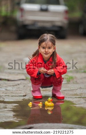 little girl  in rain boots playing with yellow rubber ducks in autumn park.