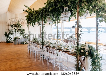 Banquet tables decorated with arrangements of flowers, herbs and candles in the tent. Wedding. Banquet.Crystal chandeliers hang from above