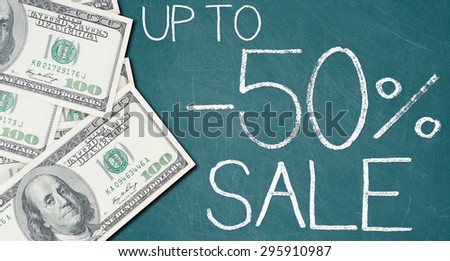 UP TO -50% SALE text written on a green chalkboard with frame made of 100 US dollars.