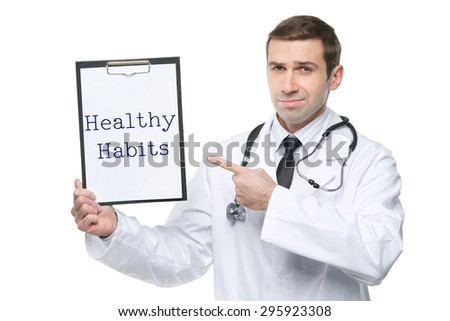 Smiling male doctor with stethoscope pointing forefinger to clipboard with HEALTHY HABITS motivational quote/ Isolated