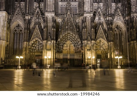 Night lighting of main portal of Dom in Cologne with walking people.