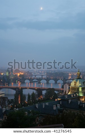 Twilight on Vltava river in Prague with bridges and moon above.