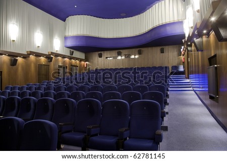 Interior of cinema auditorium with balcony and lines of blue chairs. Side view.