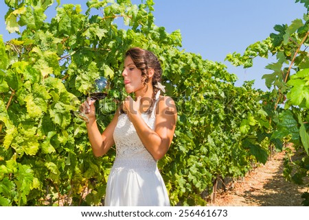 Young woman farmer tastes a glass of red wine in the vineyard.