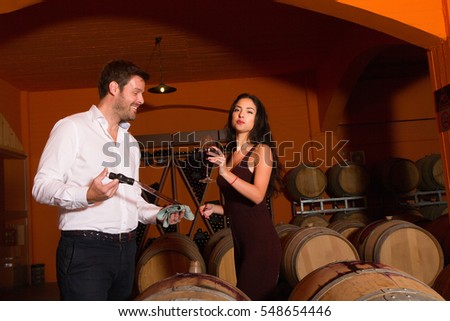 Winemaker sampling red wine for woman visitor in winery cellar. Imagine de stoc © 