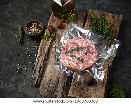 On the wooden table is a fresh frozen steak in a vacuum package. Near spices and herbs