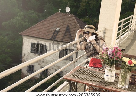 Smiling Italian Woman in Hat with paper Plane on Balcony