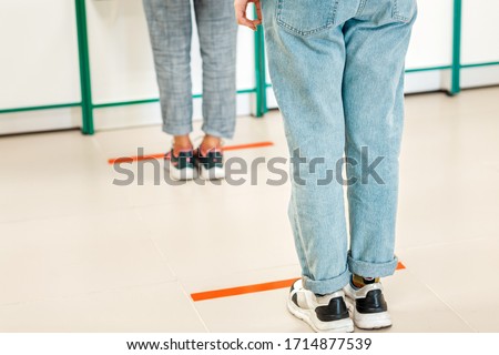 People stand in line, legs close-up. Attention line on the floor of the store to maintain social distance. Concept of the coronavirus pandemic and prevention measures