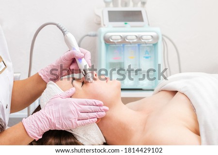 Beauty salon. The cosmetologist in medical gloves doing a hydra peeling procedure on the client's cheeks. Side view. Professional skin care and treatment concept Foto stock © 