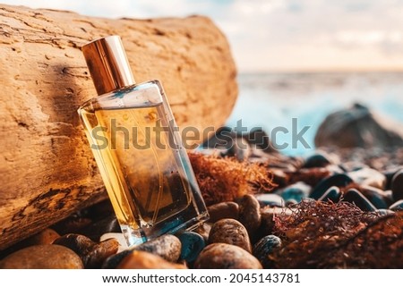 A golden transparent perfume bottle with drops on a wet pebble beach. Close-up. In the background, the ocean. Perfume and fashion advertising concept.