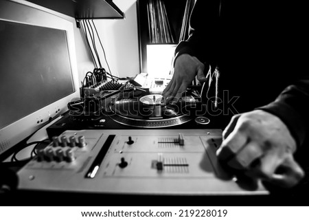 Dj in studio uses turntable and mixer for scratching. Black and white image