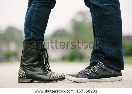 Knees down photo of a couple in an embrace facing each other in jeans and bad ass leather shoes.