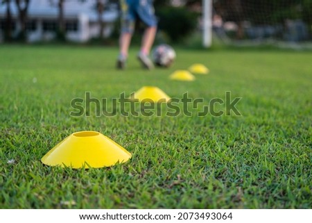 Football training cone on firm ground pitch, with action of a boy is practice football as blurred background. Sport equipment object - challenge activity scene. Selective focus at the front cone. 商業照片 © 