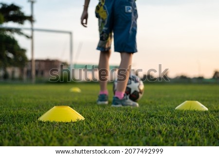 Football training cone on firm ground pitch, with action of a boy is practice football as blurred background. Sport equipment object - challenge activity scene. Selective focus at the front cone. 商業照片 © 