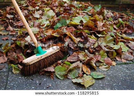 Pile of autumn leaves on backyard patio and sweeping brush