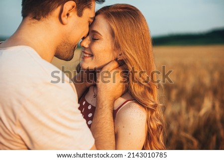 Photo of A couple touching foreheads being romantic and kissing while posing under sunlight with a blurry background. Love and relationships outdoors.