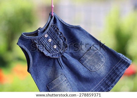 Fashion denim baby dress hanging on a hanger on a green background