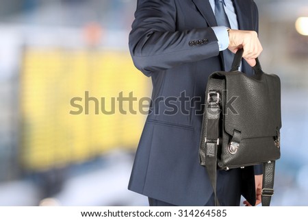 businessman  holding leather briefcase checking time on his watch at the airport
