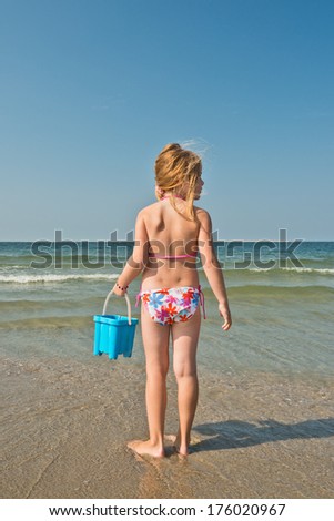 A young girl at the beach holding a pail.