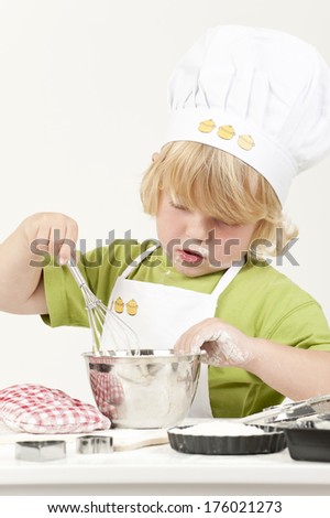 A young boy in chef hat mixing something in silver bowl.