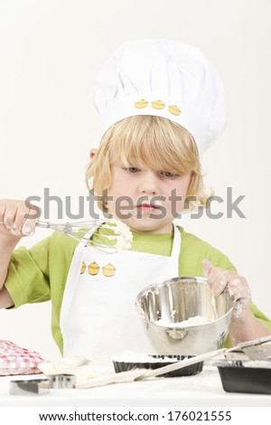 A young child baking something, while wearing a chef hat and apron.
