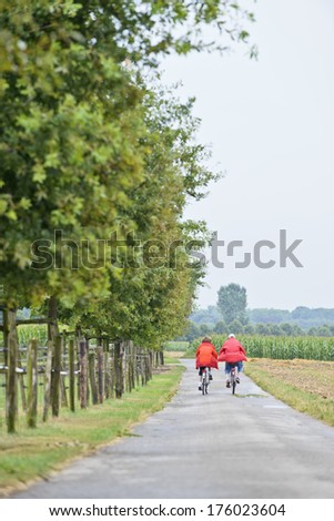 A couple riding bikes on path lined by trees and open space.