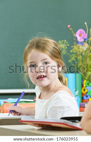 A girl at a desk holding a purple pencil with flowers and books behind her.