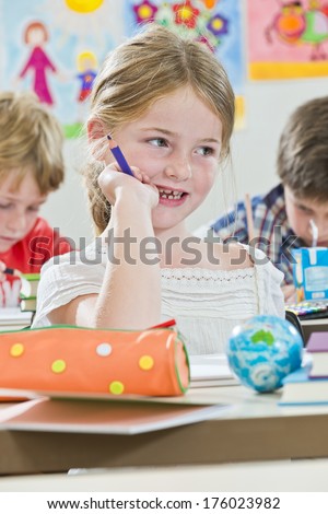 A girl at a desk with a pencil case and a purple pencil in hand.