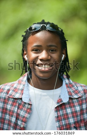 An African American youth with ear buds in and sunglasses on his head.