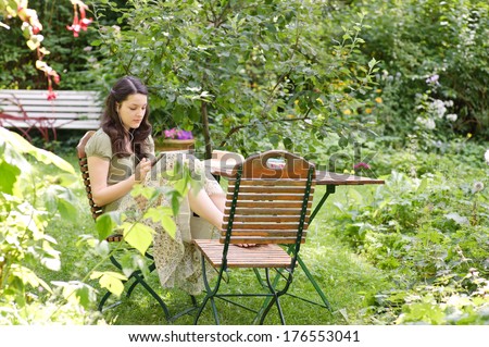 A female sitting outside on a chair next to a table in the yard.