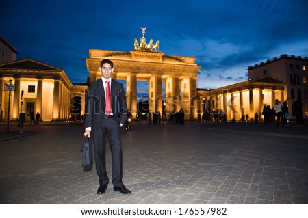A man in a suit and tie stands in front of an old building.