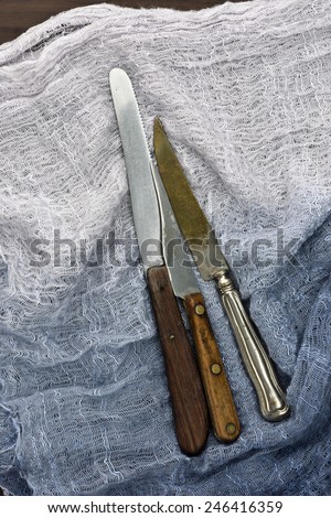 old kitchen knifes with wooden handles and one silver knife on a linen sheet