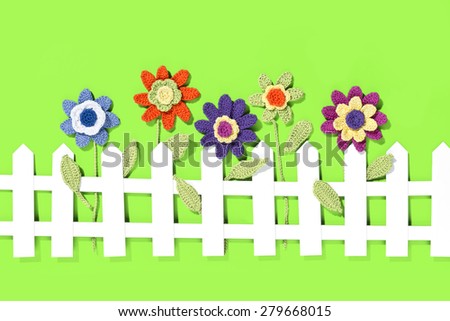 crochet flowers behind a white paper fence on green background