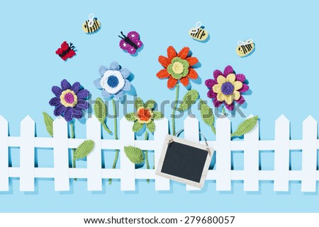crochet flowers behind a white paper fence with a tag and bees, butterflies on blue background