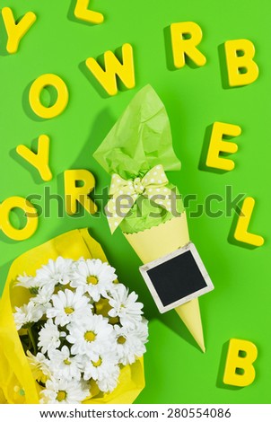 little cone present with a small blackboard tag, a bouquet of daisies and yellow letters on green background