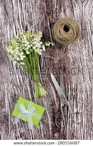a bouquet of Lily of the Valley with a present, scissors and a cord on a wood textured imitation