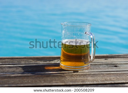 Plain pint glass of cold lager beer sitting on edge of blue swimming pool