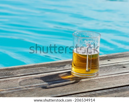 Plain pint glass of cold lager beer sitting on edge of blue swimming pool