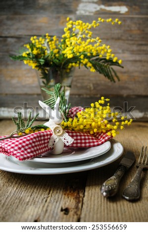 Spring festive dining table setting with yellow mimosa flowers, candles, napkins and vintage cutlery on a wooden board