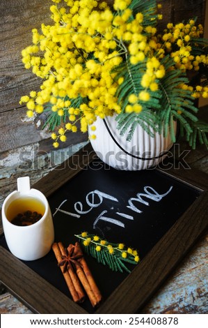 Glass cup with tea and blooming yellow mimosa with good morning note on wooden background
